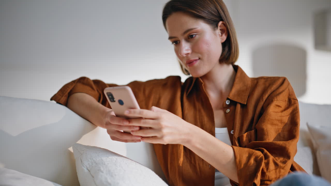 Lady chatting online mobile phone sitting modern light sofa closeup smiling