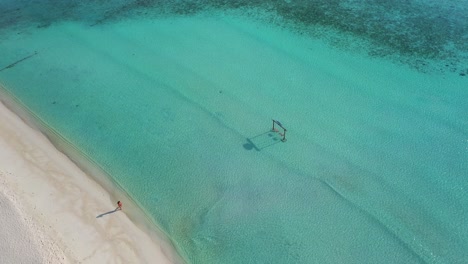Vista-Aérea-De-Una-Mujer-Solitaria-Caminando-En-La-Playa-De-Arena-Blanca-De-La-Isla-De-Maldivas-Junto-Al-Agua-Turquesa-Del-Océano