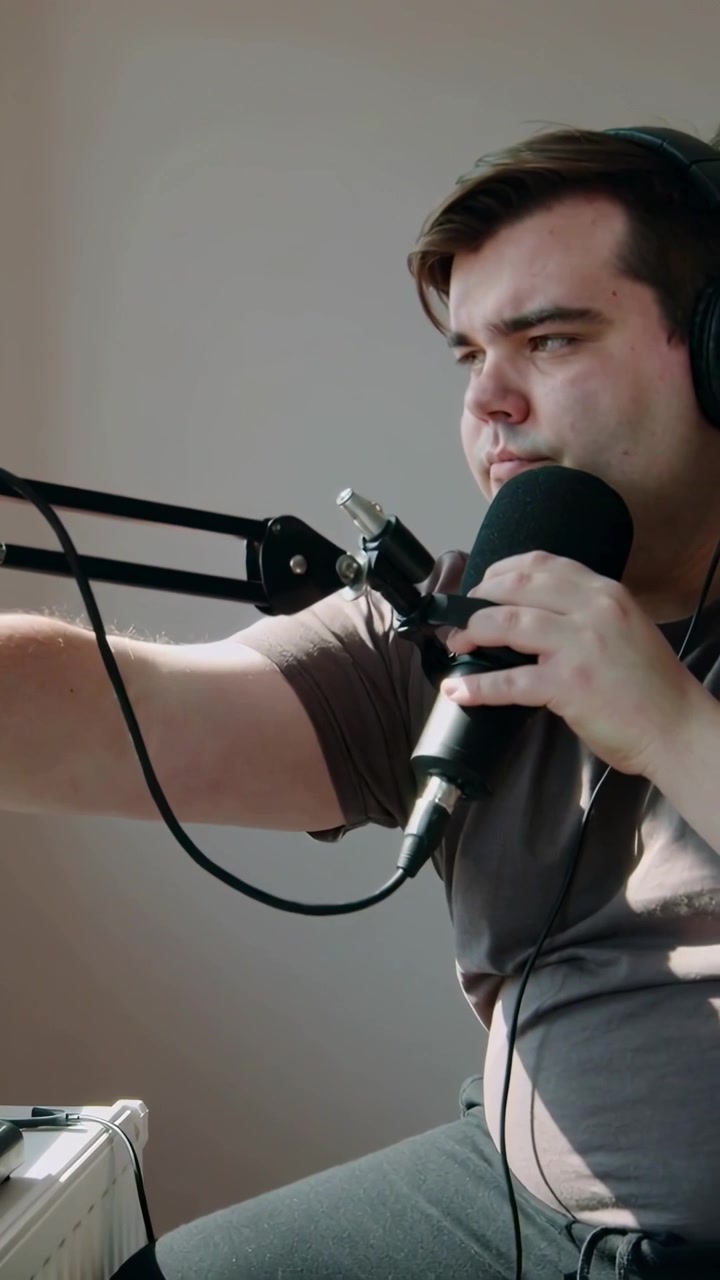 Video verticale: Uomo in maglietta che si prepara a registrare, regola il microfono e indossa le cuffie in studio, spazio per il testo.