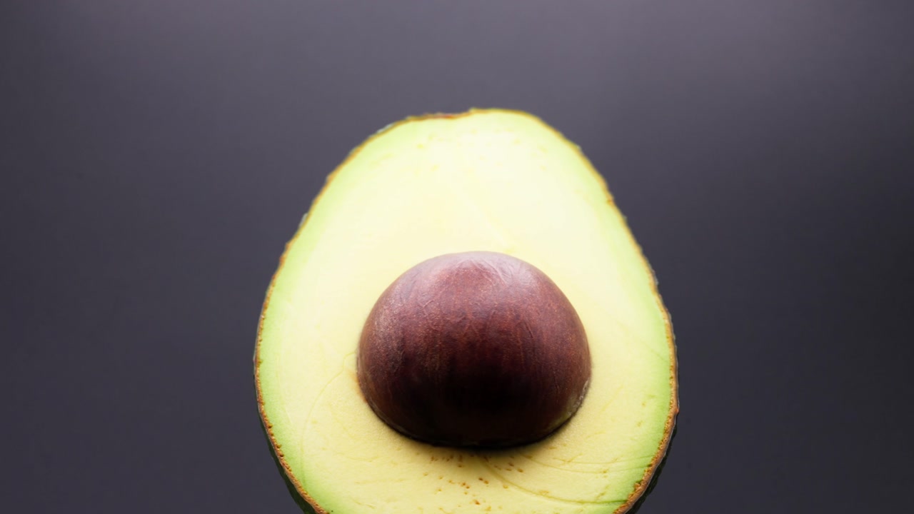 CLOSE UP SHOT OF AN AVOCADO ROTATING ON A BLACK BACKDROP