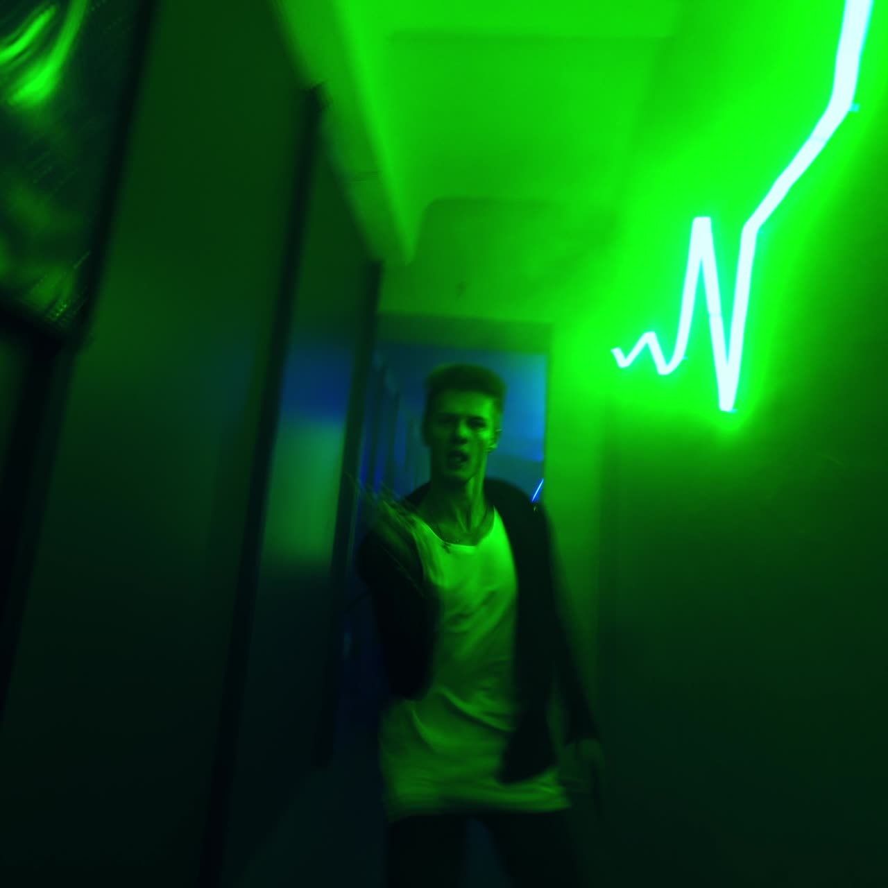 Young man dances in the long narrow corridor. Hip hop dancer performs in the green light hall