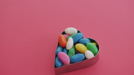 video of overhead view of multi coloured sweets in heart shape over red background