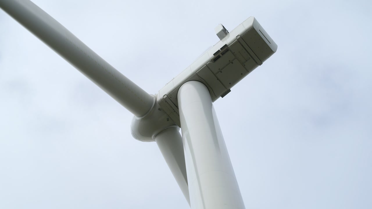 Static shot beneath a wind turbine looking up at its hub and spinning blades.