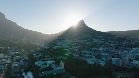 Rising-sun-behind-tall-peak-above-residential-borough.-Lions-Head-mountain-casting-shadow-on-town.-Cape-Town,-South-Africa