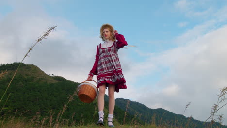 low angle view of young blonde female model in tradition old fashioned clothing style while holding food basket and walking in nature