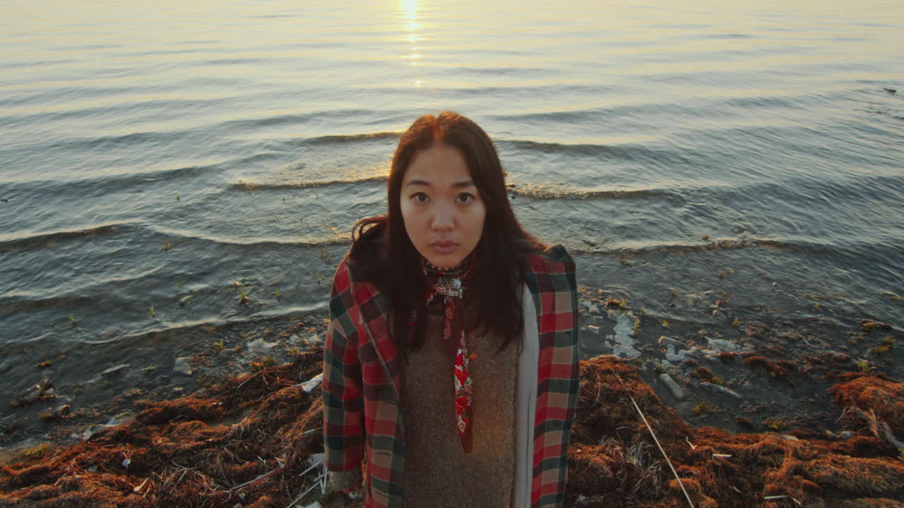 해가 지는 동안 호수 연안에 서 있는 젊은 아시아 여성의 초상화