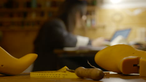 Various-shoemaker-tools-on-workbench-in-foreground-with-designer-working-blurred-out-in-background