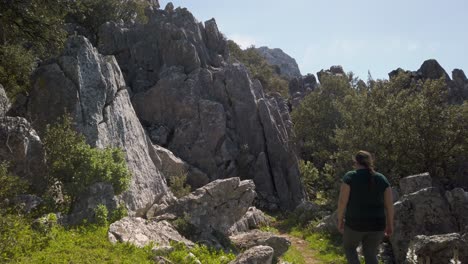 Woman-walks-alone-on-hiking-trail-through-rugged-rocky-mountain-landscape