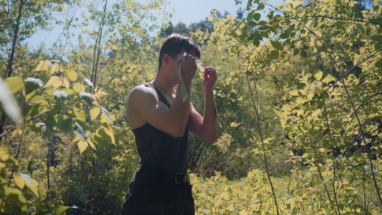 Side view of tourist unrolling white headband and tying back on head while standing in lonely forest, sunlight filtering through green leaves onto freckled skin and dark top, branches surrounding