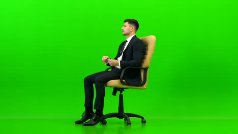 The businessman talking on the office chair on the green background