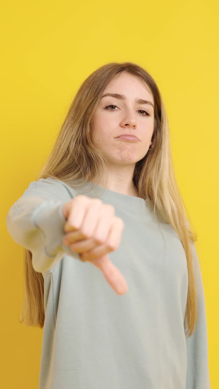 Young woman expressing disapproval with thumbs down on yellow background