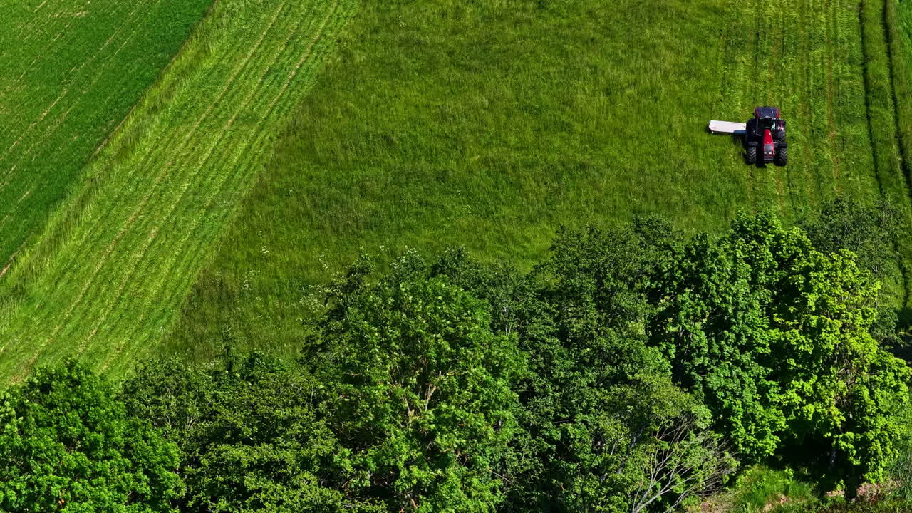 Top-down drone overview of lawn mower on lush green meadows near wetland lakes