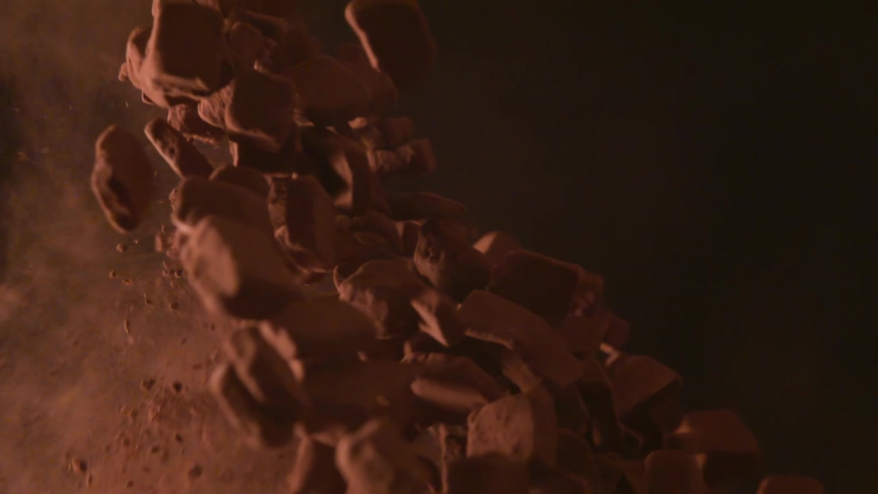 Misturando cubos de chocolate com cacau em pó fino, em um fundo preto, em uma tigela prateada 4K