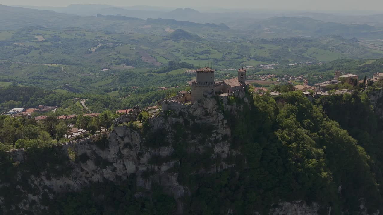 Wide drone shot of La Rocca (Guaita Tower) perched on Monte Titano in San Marino. This iconic medieval fortress dominates the skyline and offers a breathtaking view of the surrounding countryside.