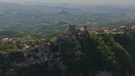 wide drone shot of la rocca (guaita tower) perched on monte titano in san marino. this iconic medieval fortress dominates the skyline and offers a breathtaking view of the surrounding countryside.