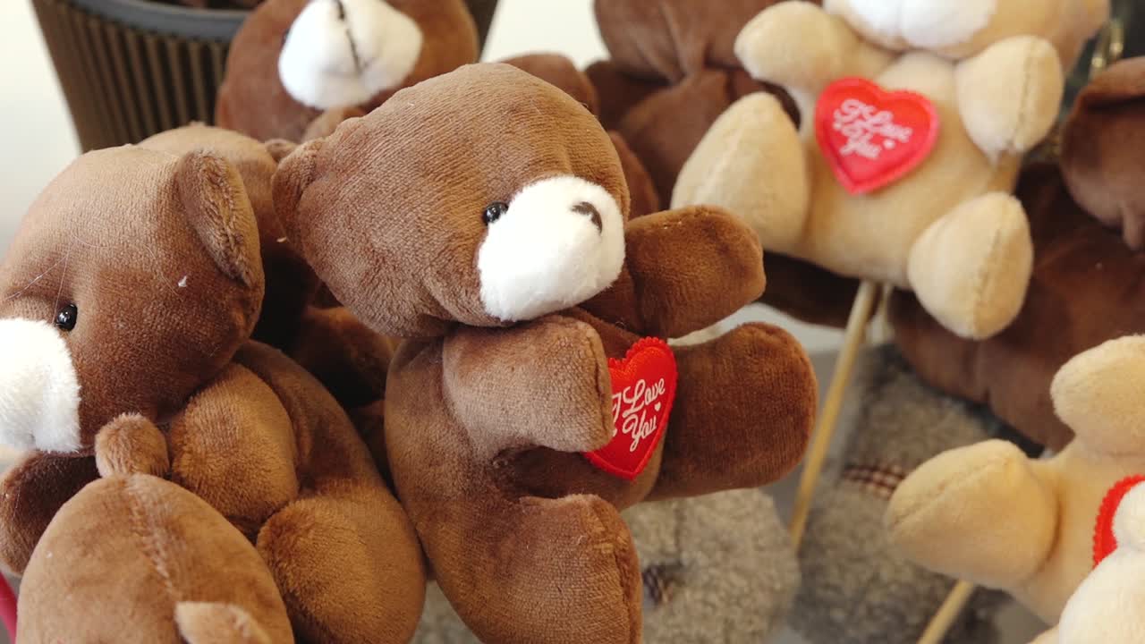 Close-up de ursinhos de pelúcia marrons macios exibidos com etiquetas de coração vermelho com os dizeres “Te Amo”. Itens de presente fofos arranjados em ambiente interno, simbolizando romance e afeto.