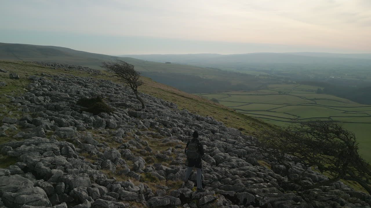 excursionista admirando la vista sobre la ladera rocosa con un horizonte brumoso en la campiña inglesa en ingleton, yorkshire, reino unido