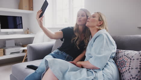 senior mother with adult daughter sitting on sofa posing for selfie on mobile phone