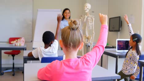 Schulkinder-Heben-Die-Hand,-Während-Sie-In-Der-Grundschule-Am-Schreibtisch-Sitzen,-4k