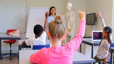 escolares levantando la mano mientras están sentados en el escritorio en la escuela primaria 4k