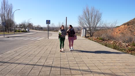 two women walk home from gym, chatting on sunny winter day. wide static shot, 4k
