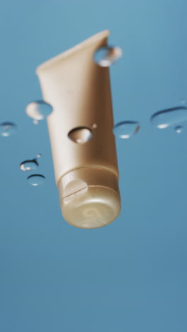 vertical video of drops falling on beauty product tube with copy space on blue background