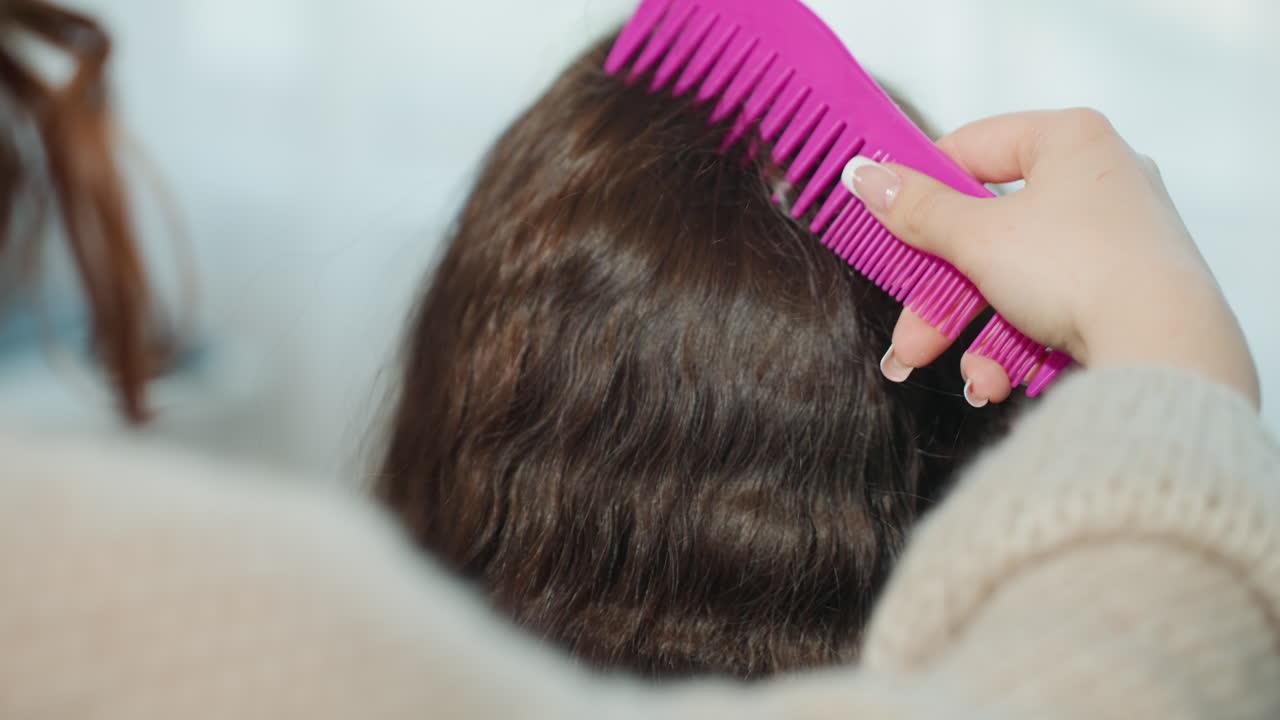 WideShot Combing Wavy Brown Hair By Stylist Hand In Cozy Sweater, Pink WideTooth Comb Smoothing Waves, Client Seated In Chair, Ambient Salon Blur, Steady Professional Preparation For Cut