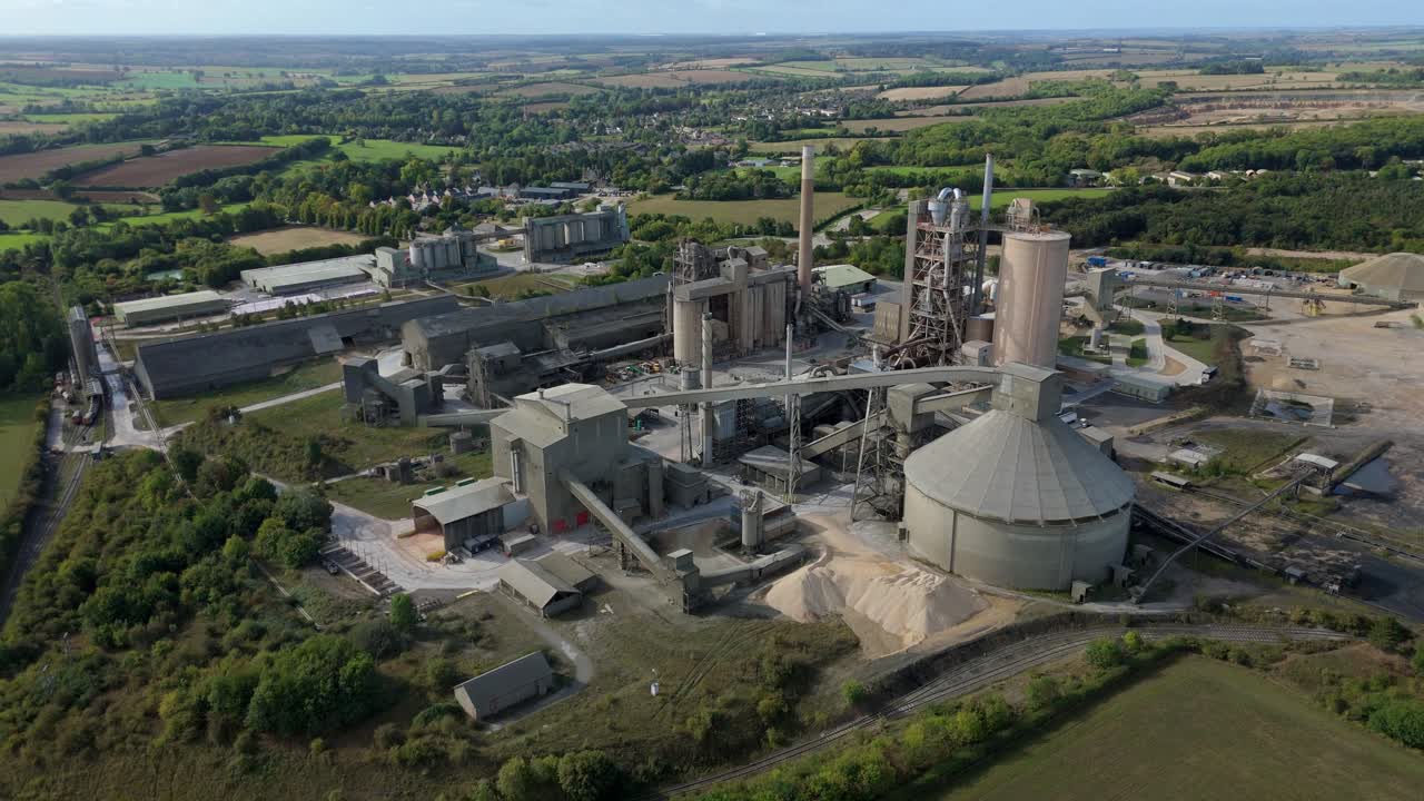 Aerial drone footage of cement factory with chimneys, pipework, and smoke stacks near Stamford on a sunny day in central England