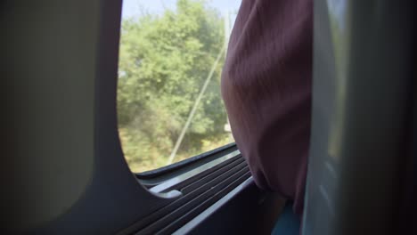 passenger sitting next to train window while travelling through rural landscape