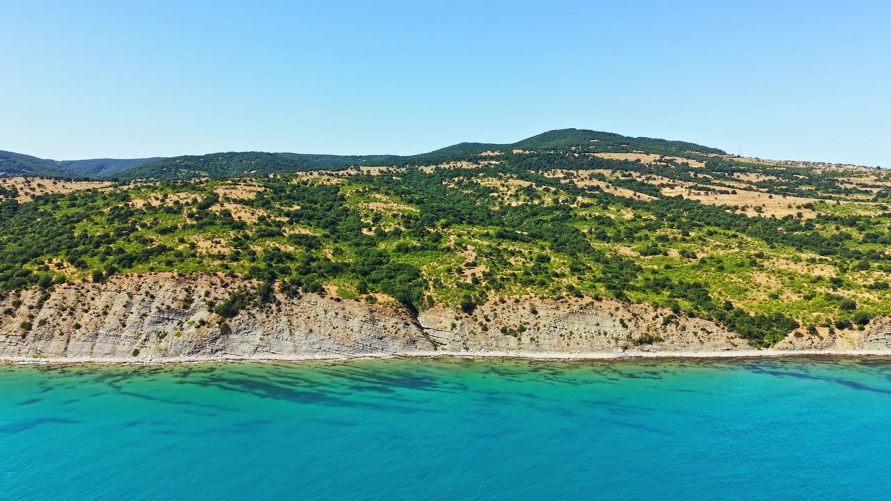 Bilinmeyen bir konumda, yaz mevsiminde öğle vakti kumlu bir plajın yakınında yeşil tepeler ve mavi su ile kıyı şeridi.