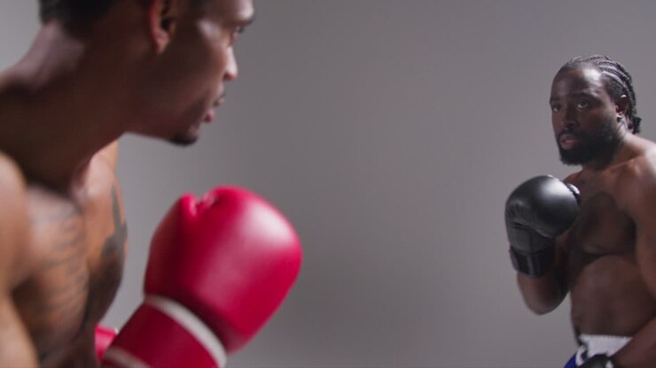 Scatto in studio di azione in tempo reale di due pugili maschi che indossano i guantoni e combattono in un incontro di boxe su sfondo grigio 2