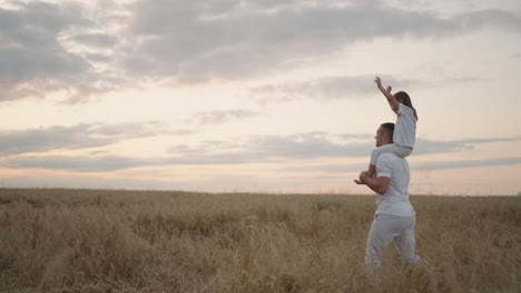 happy child and father are playing in field of ripening wheat. little daughter on fathers shoulders. baby boy and dad travel on field. kid and parent play in nature. happy family and childhood concept