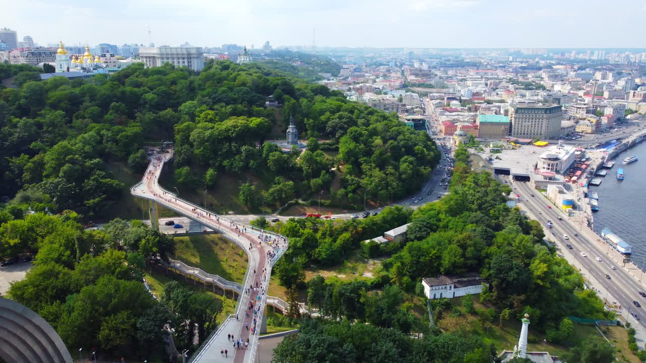 Recently built pedestrian-bicycle bridge over Vladimirsky descent and Peoples' Friendship Arch cinematic landscape. Drone panning to reveal spectacular view of Kyiv, and wide Dnipro river