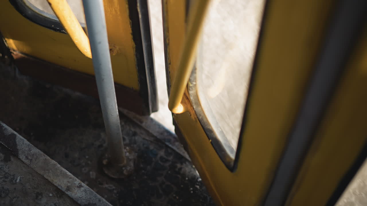 high angle view of partially open moving train door, winter light across worn steps, yellow frame, metal pole and handle visible, urban snow blur outside, tense transit moment during slow stop