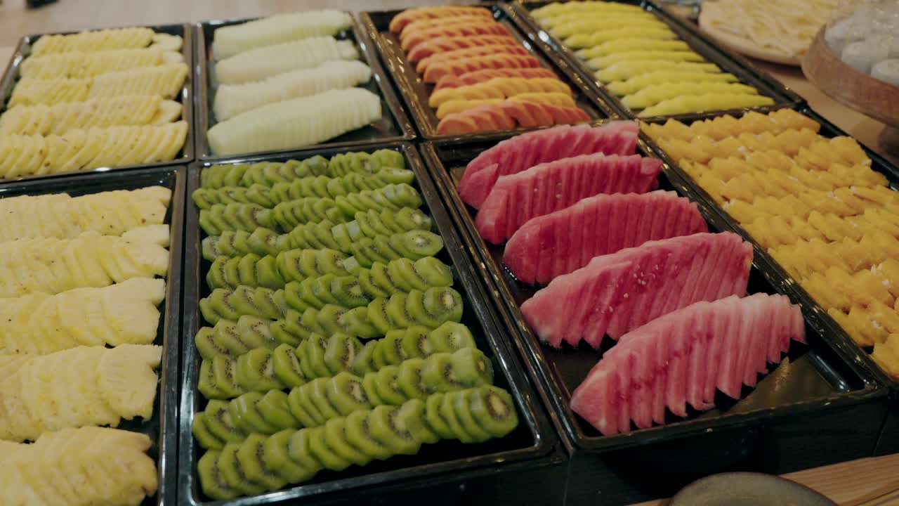 Neatly arranged trays of sliced fruits, including watermelon, kiwi, pineapple, and mango.