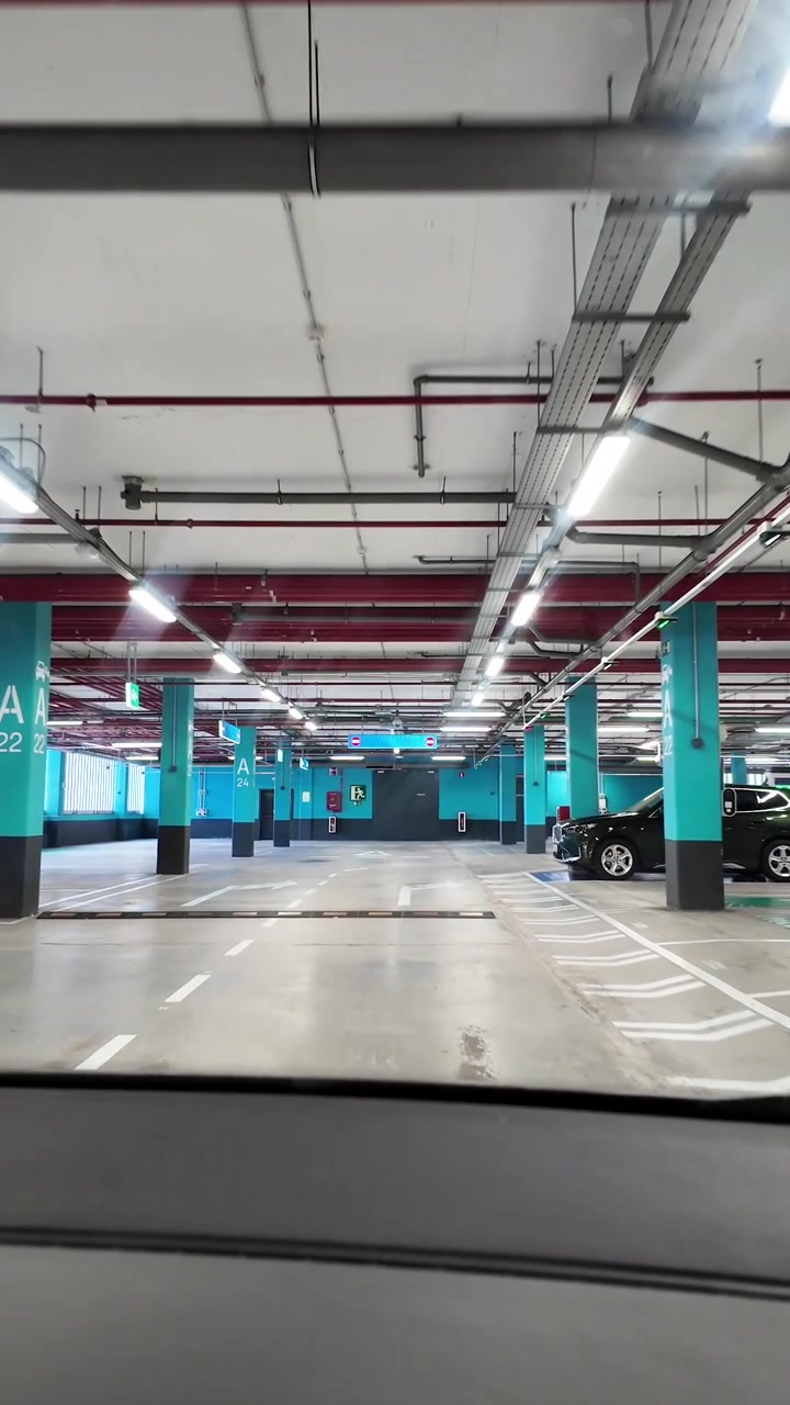 Bil kører gennem indendørs parkeringshus, set indefra.