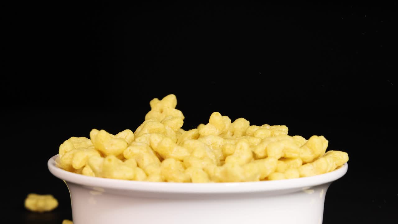 Star-shaped cereal pieces drop into a white bowl against a dark backdrop, highlighting motion and texture in a controlled setting