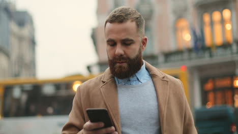 Hombre-De-Negocios-Caucásico-Con-Barba-Enviando-Mensajes-De-Texto-Por-Teléfono-En-La-Calle-En-Otoño