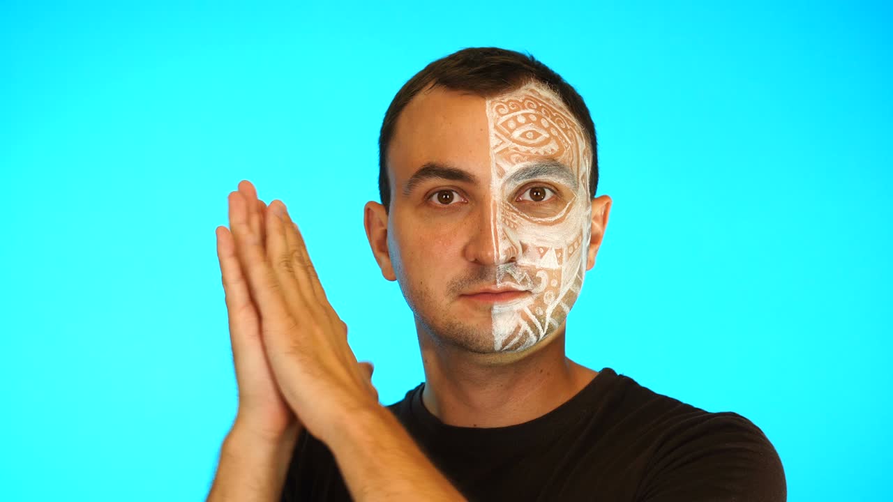 Man with painted looking at camera and applauding against blue background