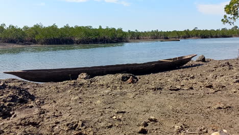 Handcrafted-canoe-made-of-tree-trunk,-on-top-of-dry-mud-at-low-tide-on-the-Indomar-river-in-Quinhamel,-Guinea-Bissau