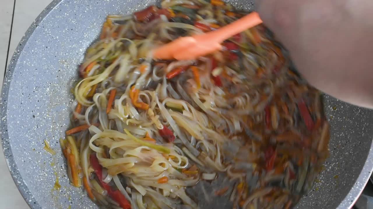 mano de hombre revolviendo fideos y verduras picadas mientras se fríe en un wok