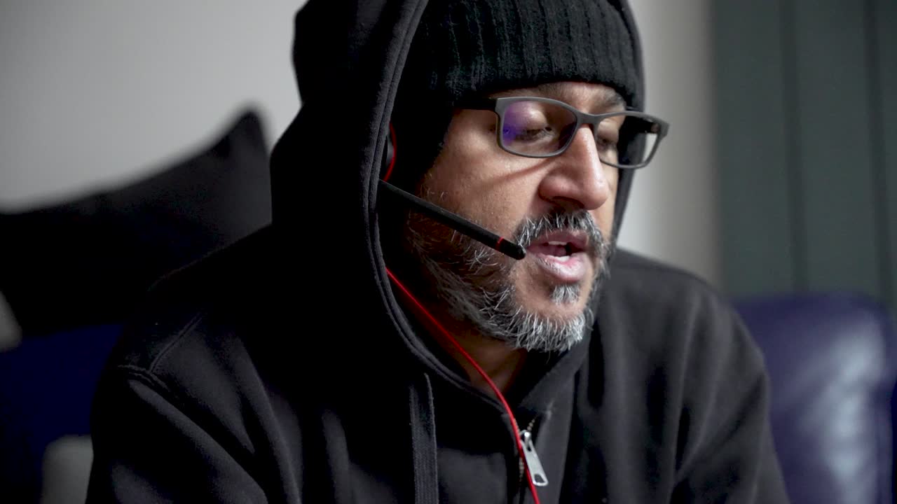 South Asian Male Wearing Headset And Glasses Working From Home Freelancer In Hoodie And Beanie Remote Worker Home Office
