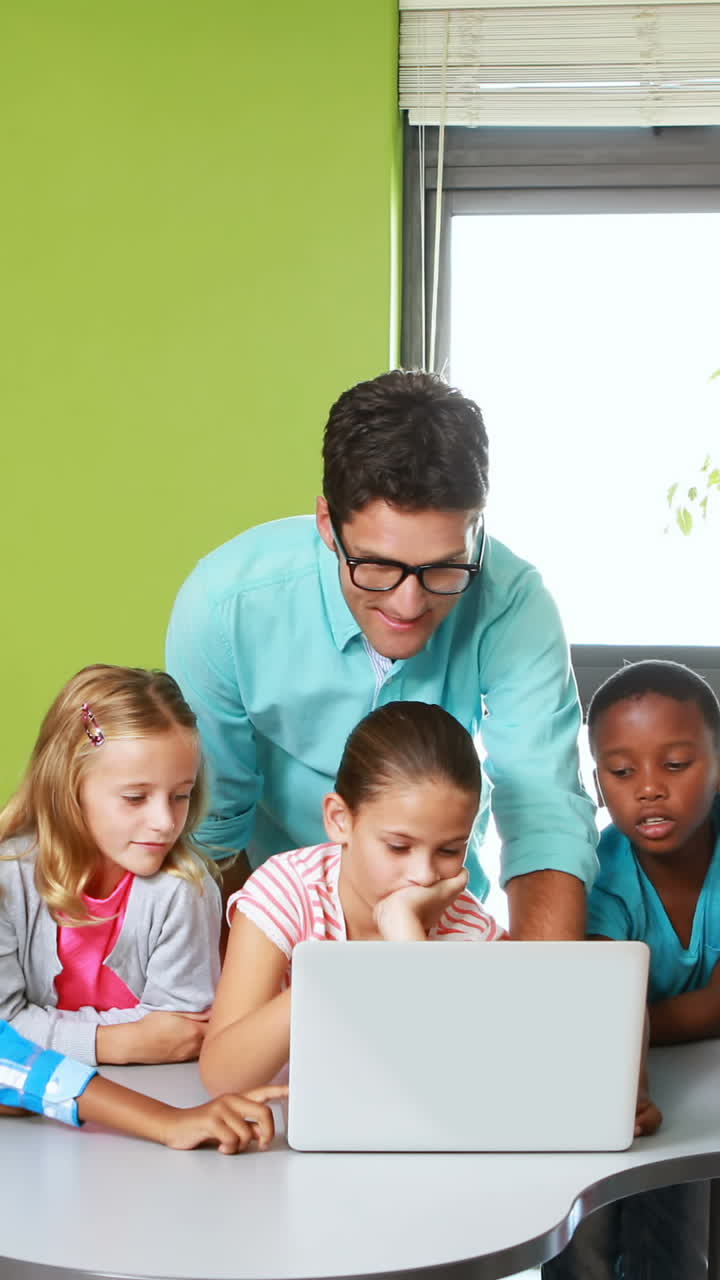 el maestro y los niños usando la computadora portátil en el aula