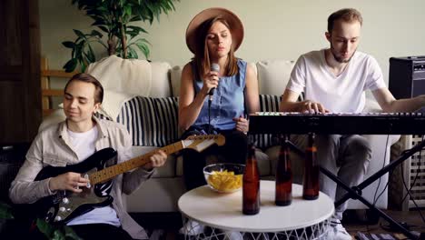 vocalist pretty blonde is singing and snapping fingers while her friends and colleagues from musical band are playing the keyboard and the electric guitar.