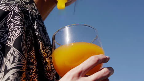 a person pouring and drinking orange juice under a clear blue sky