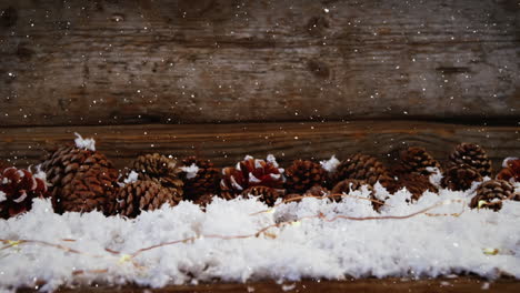 video composition with falling snow over desk with pine cones on snow