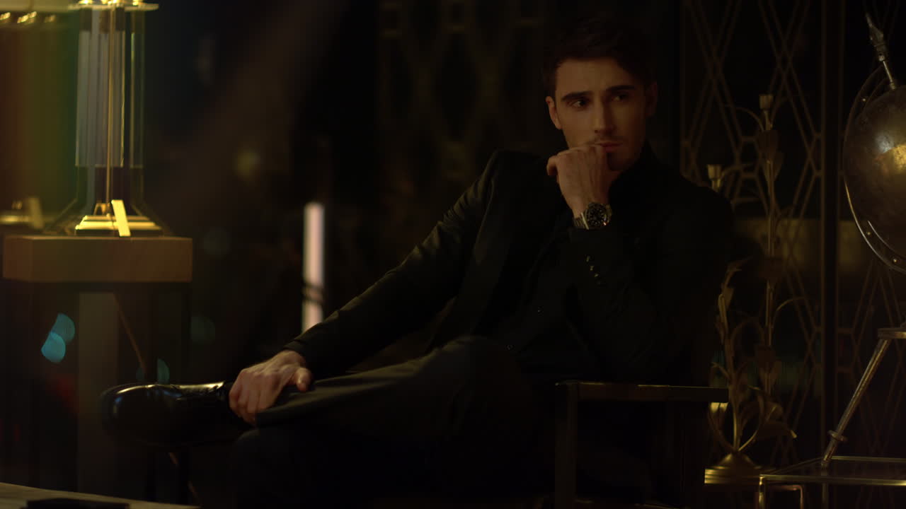 어두운 방에서 다리를  ⁇ 고 앉아 있는 부자. 무언가를 고민하는 스타일리쉬한 남자