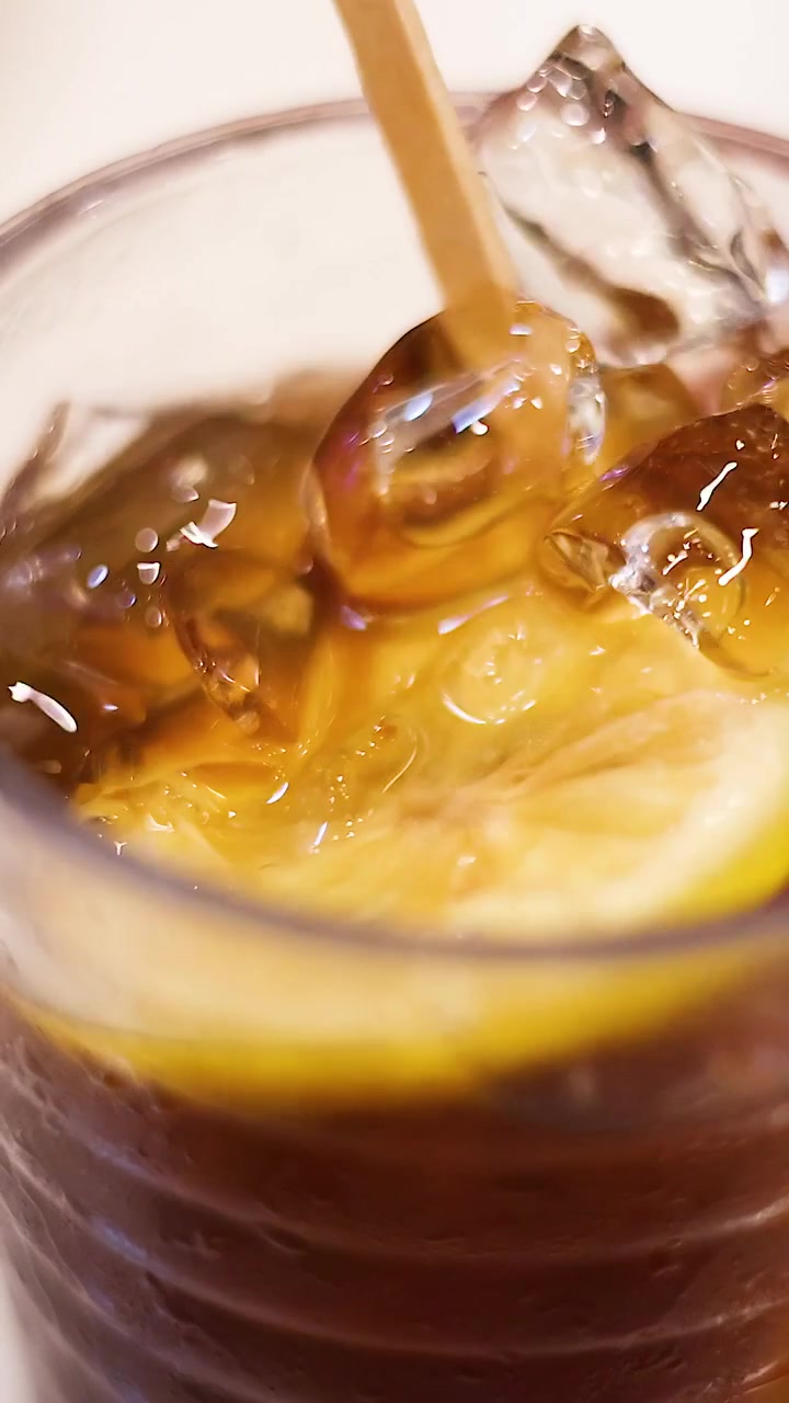 Mano che mescola tè freddo con limone e ghiaccio