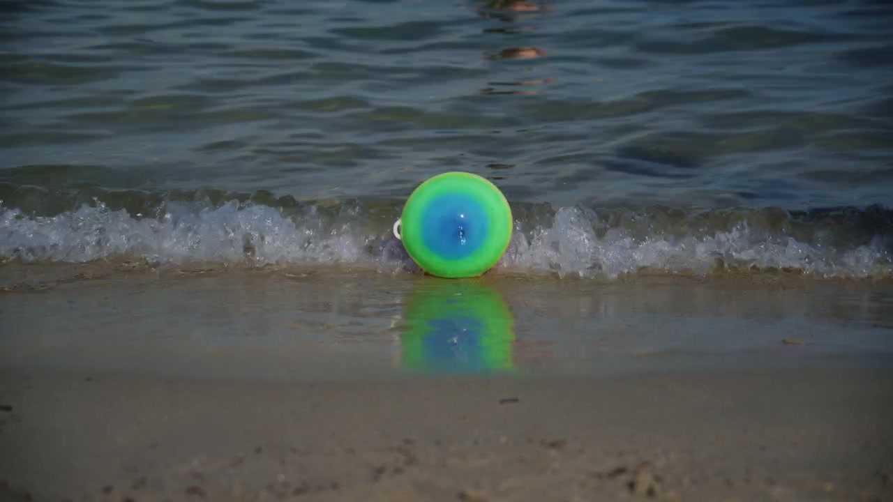 Colorful beach ball floating at the edge of gentle waves on the sandy shore of Plage de la Gravette in Antibes, France, during a sunny summer day on the French Riviera