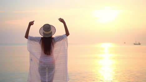 una mujer encubierta se para frente al sol poniente levantando los brazos con alegría